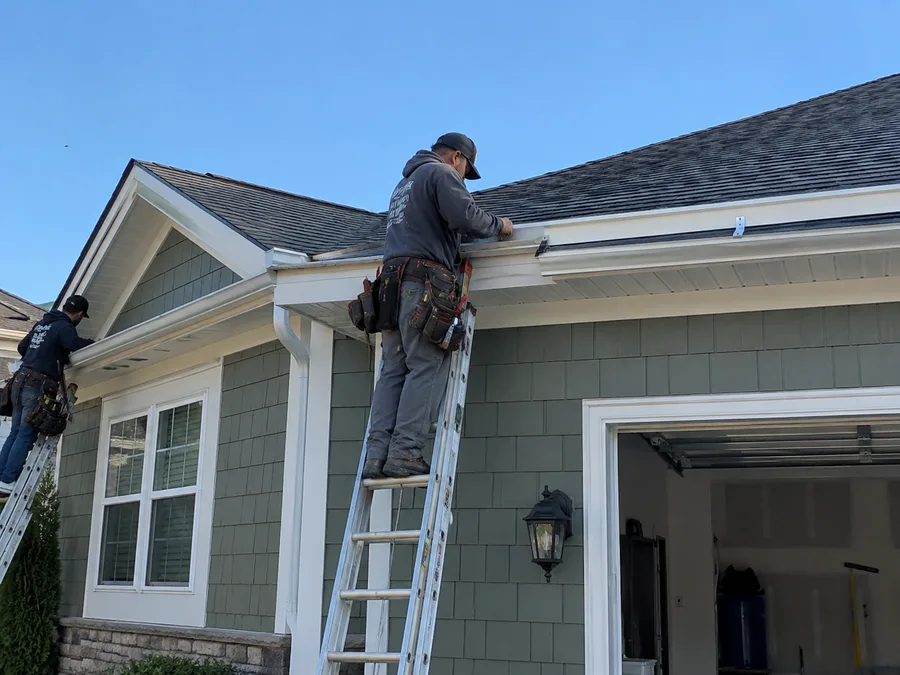 Roofer installing new gutters along a roofline
