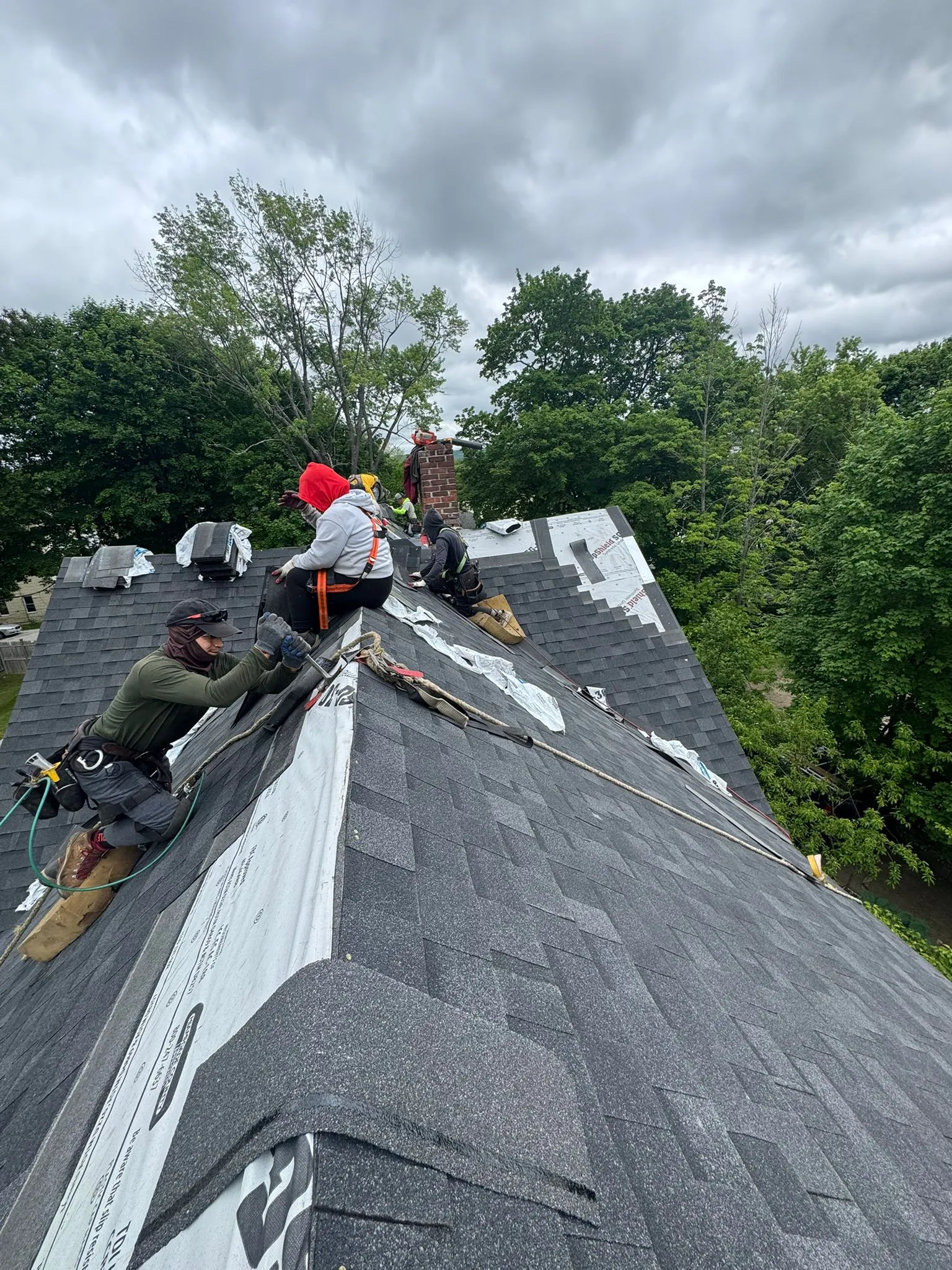 Professional roofing contractors installing asphalt shingles on residential home in Manchester NH